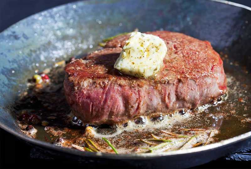 Un steak en train de cuire dans une poele avec du beurre dessus