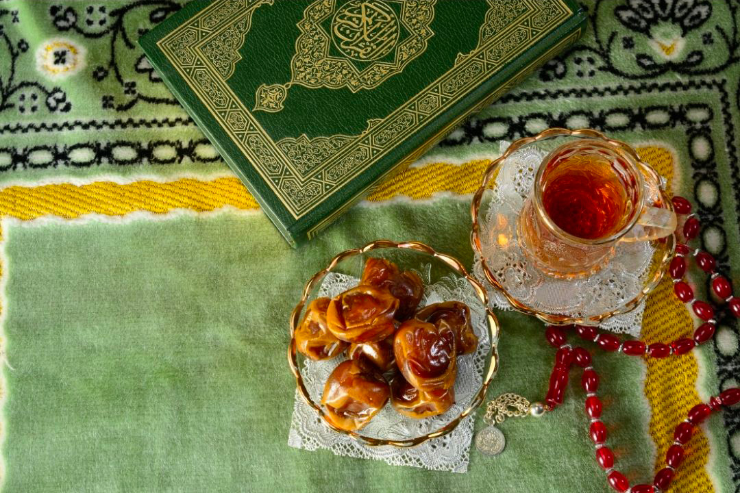des dattes dans un bol avec une tasse de thé sur une table avec une nappe verte décorée pour le ramadan