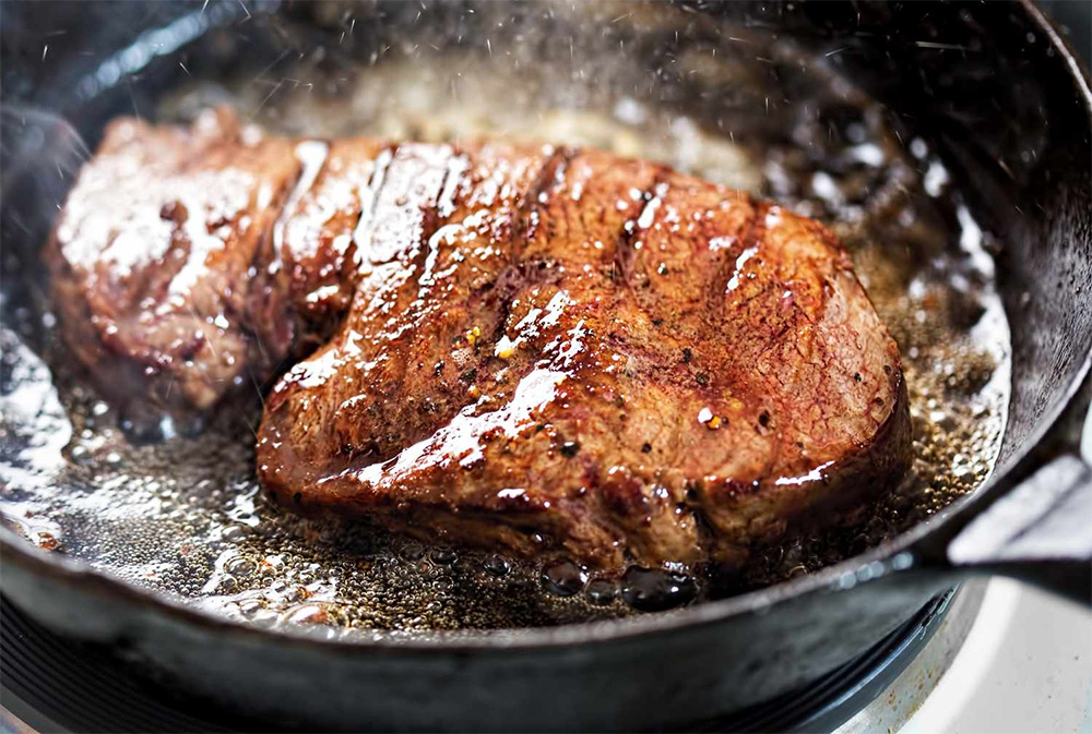 Un steak en train de cuire dans une poêle avec de l'huile