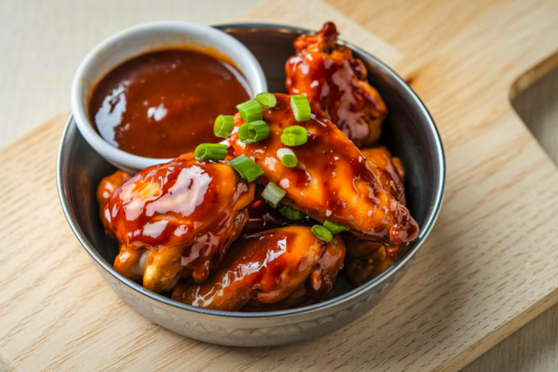 Une sauce barbecue dans une petit bol accompagnée d'ailes de poulet grillées