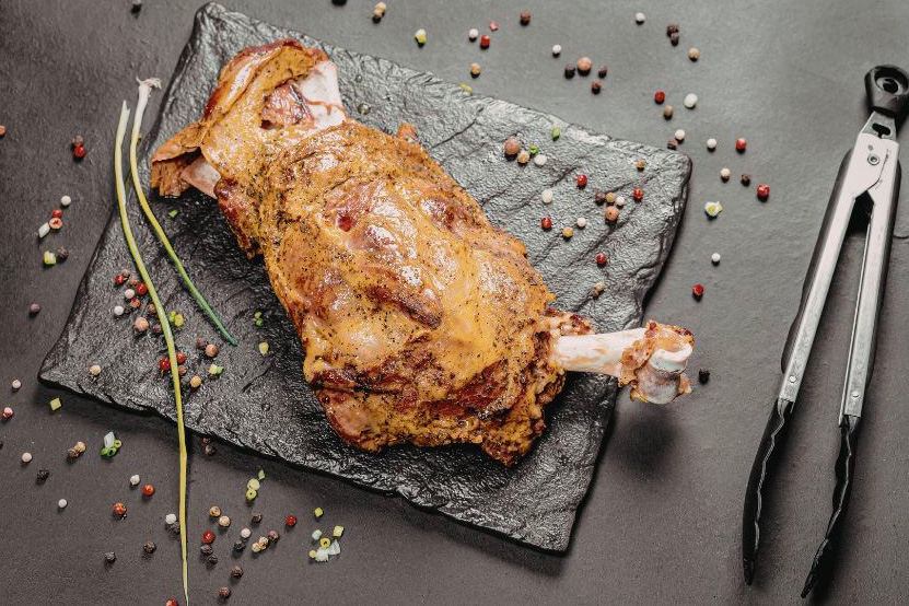 Une épaule d'agneau confite placée sur une assiette en ardoise
