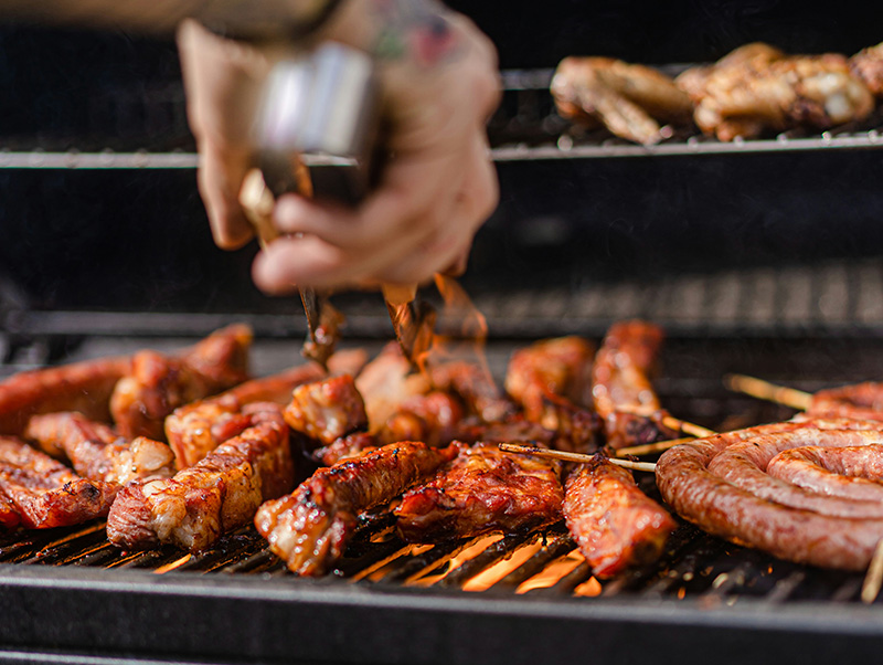 Une personne en train de retourner de la viande avec une pince su une grille de barbecue