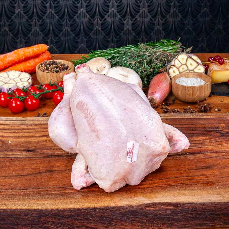 Un poulet entier prêt à cuire cru posé une une planche en bois