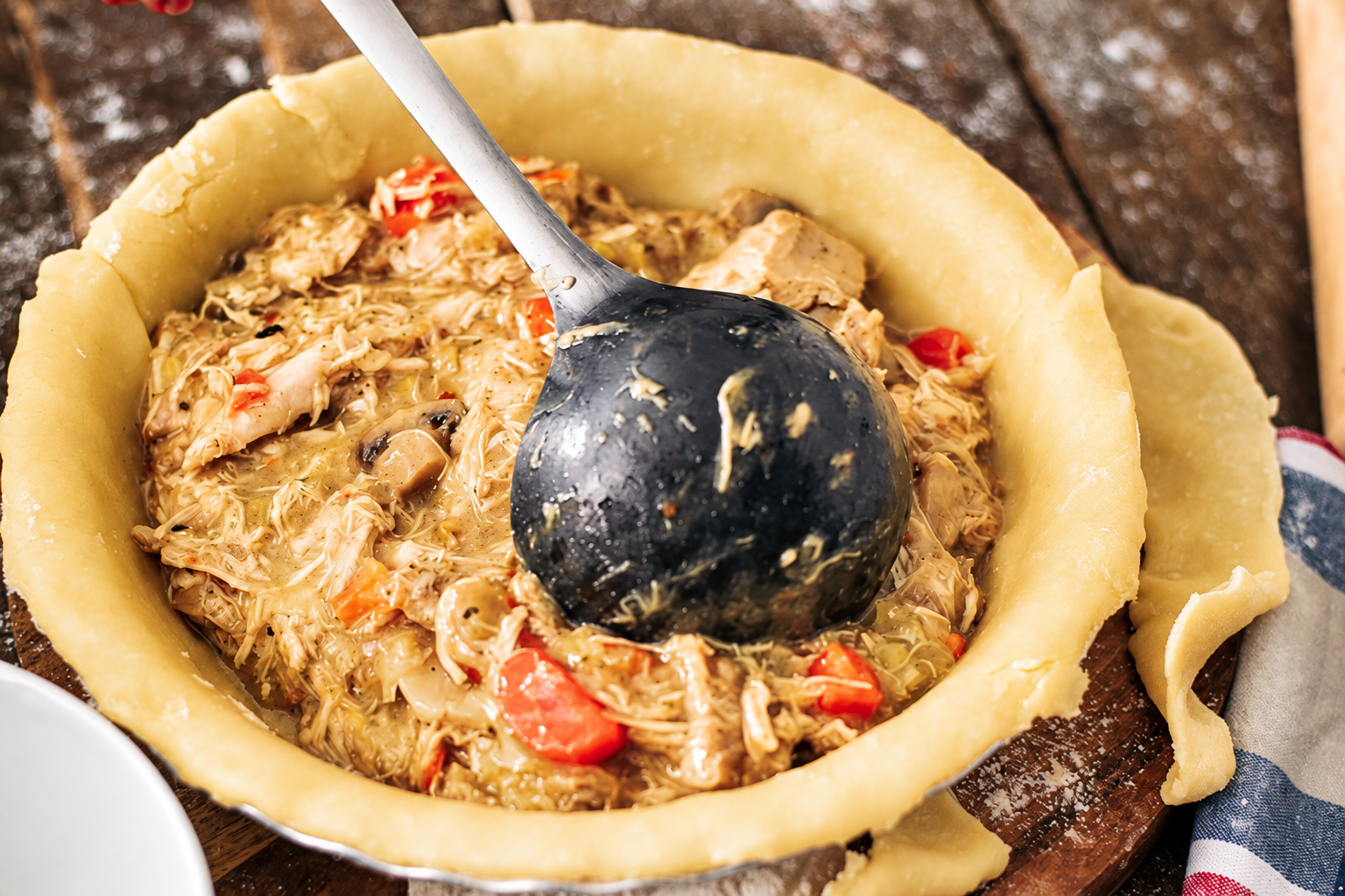 Une louche qui dépose de la viande poulet effilochée dans la pâte d'une tourte