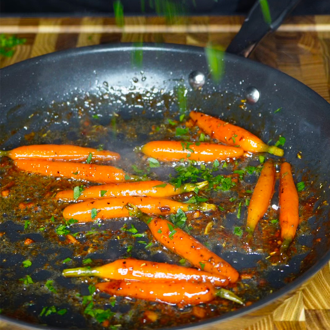 Des carottes glacées dans une poêle en train d'être assaisonnées avec du persil