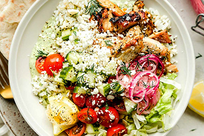 Un bowl de poulet avec de l'aneth des tomates et du concombre et du riz servi dans un bowl