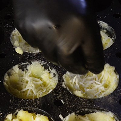 Une main qui met de l'emental dans un moule à muffin