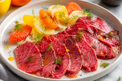Un gravlax de boeuf servi dans une assiette blanche avec des agrumes