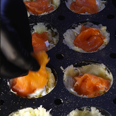 Une main qui met une petite tranche de saumon dans un moule à muffin