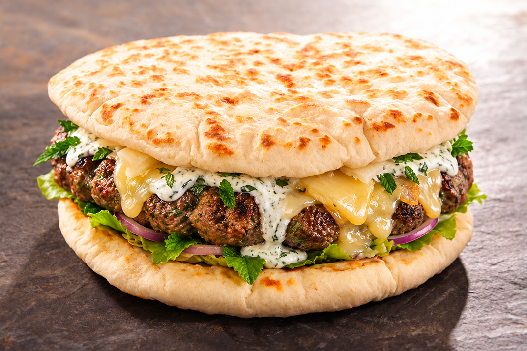 un burger réalisé avec du pain pita garni de kefta de boeuf et sauce à la menthe