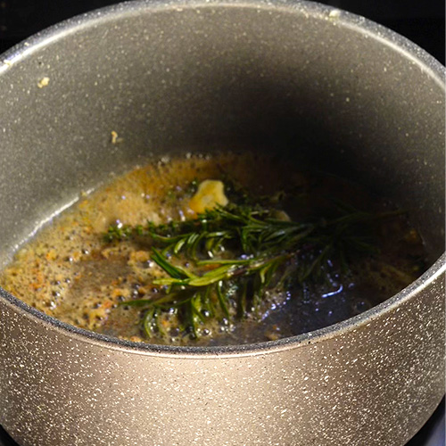 Un cocotte contenant du beurre fondu et des aromates en train de bouillir
