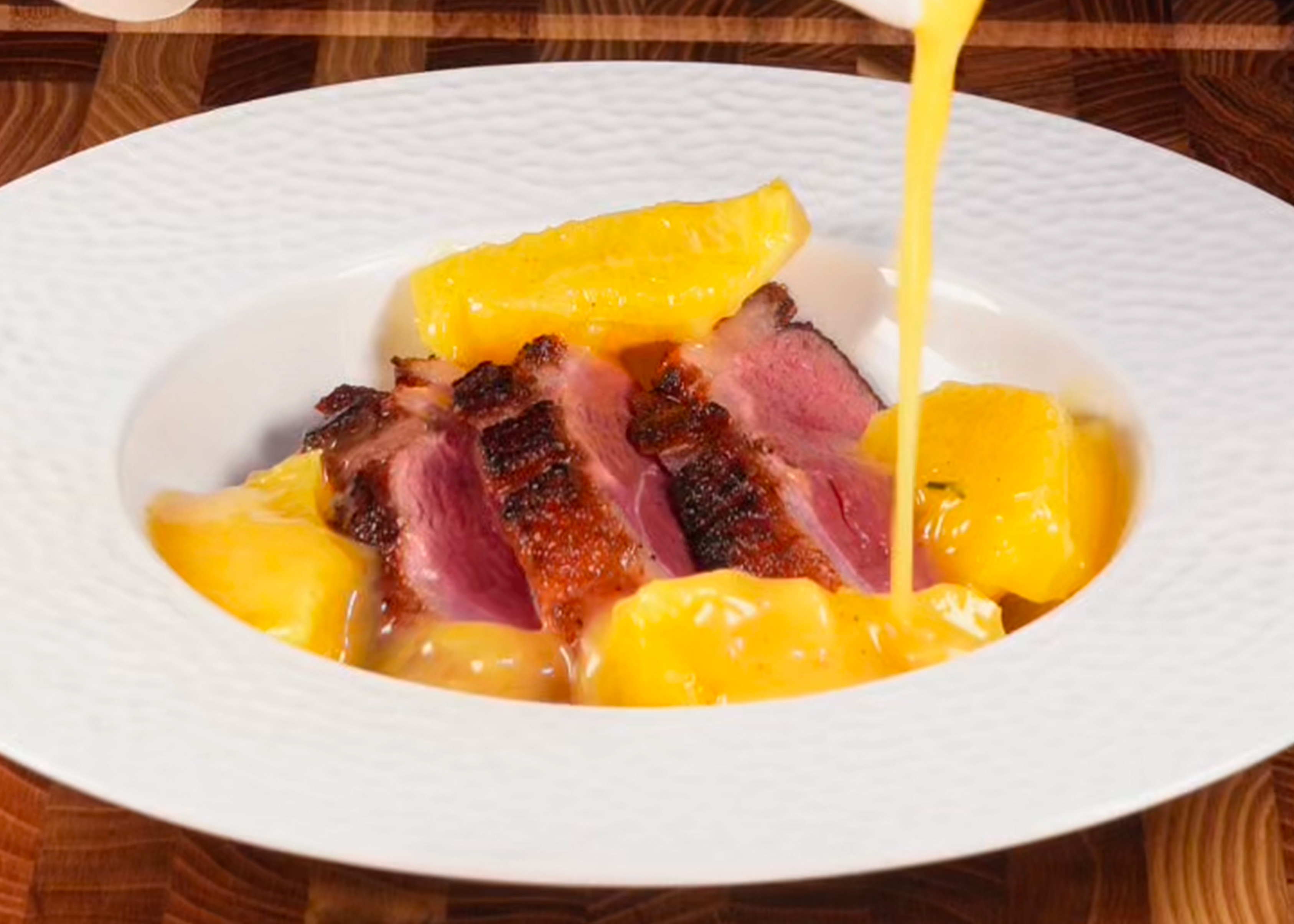 Des tranche de magret de canard rosé dans une assiette creuse blanche avec une sauce à l'orange