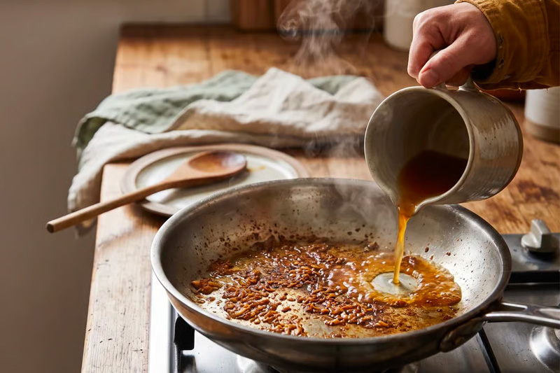 Une personne qi déglace les sucs de cuisson dans le fond d'une poêle