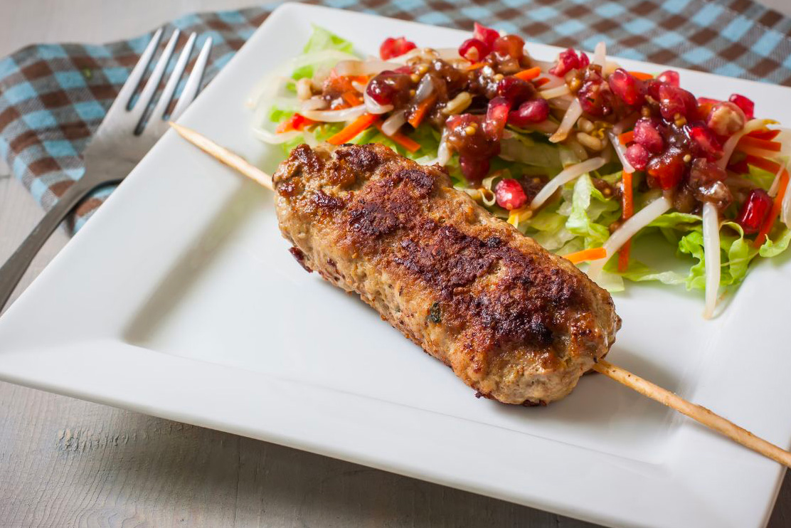 Une brochette de kefta dans une assiette blanche accompagnée d'une salade